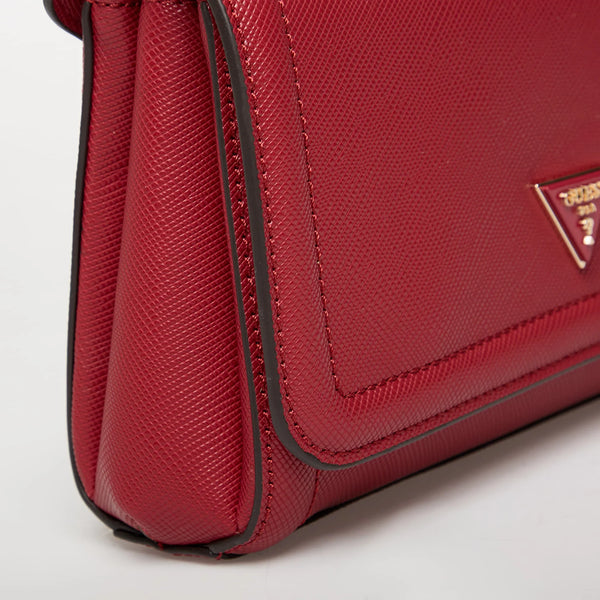 Primo piano laterale della borsa Guess Noelle rosso rubino con trama saffiano, che mostra lo spessore a soffietto del compartimento, la bordatura scura rinforzata e una parte del logo frontale a triangolo.